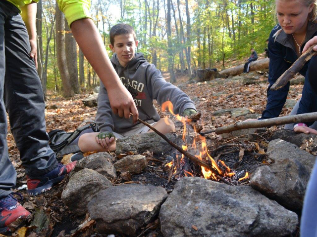 A group of campers poking at a campfire with sticks.